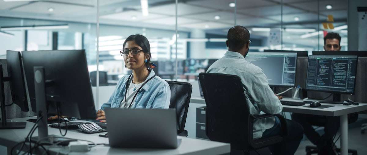 a woman sitting at a desk with a man in the background